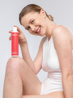 Beautiful woman holding a pink bottle of "paradigm 99" moisturizing body lotion with a white cap against a light gray background.