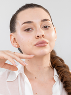 Woman with a ponytail wearing a white shirt against a plain background. Her skin looks healthy and radiant after using.