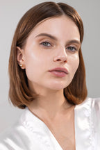 Woman with short brown hair wearing a white top against a light grey background with glow and fresh skin. 